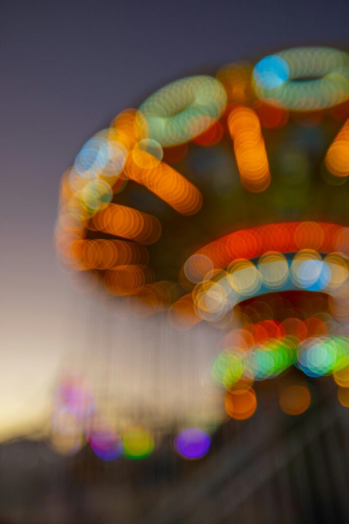 Abstract bokeh photograph of colorful carnival lights at dusk, with vibrant orange, blue, and green circles of light creating a dreamy out-of-focus effect – example of creative abstract photography using bokeh.
