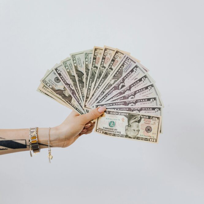 Tattooed arm holding a fan of cash, symbolizing pricing your photography and understanding real business earnings.
