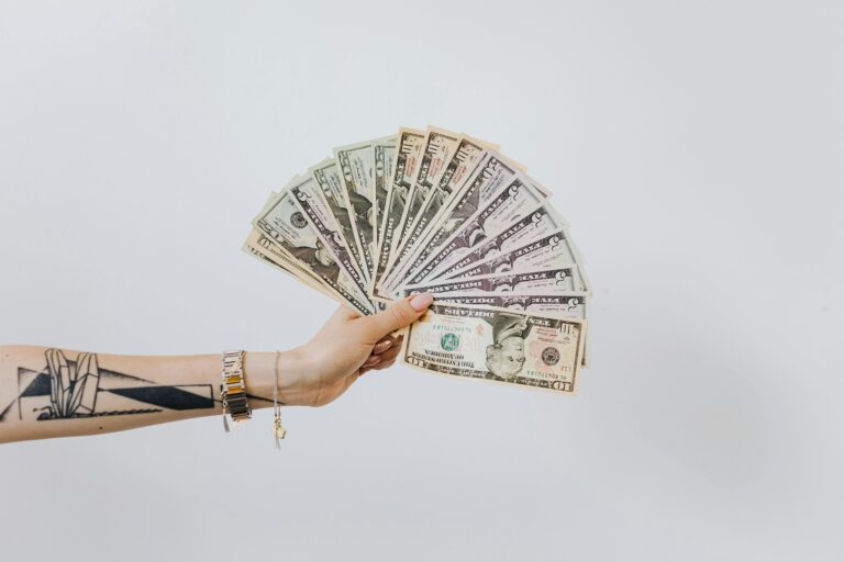 Tattooed arm holding a fan of cash, symbolizing pricing your photography and understanding real business earnings.