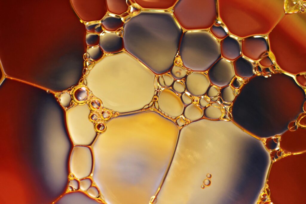 Macro abstract photograph of oil and water bubbles creating geometric shapes and colorful patterns in shades of gold, amber, and violet – creative abstract photography texture.
