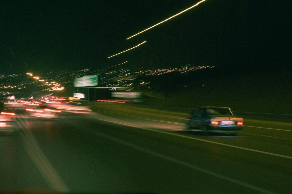 Abstract night photograph of a city highway with moving cars, captured using long exposure and motion blur—streaks of headlights and taillights create dynamic lines and a sense of speed.